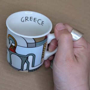 Hand holding small Greece-themed espresso cup