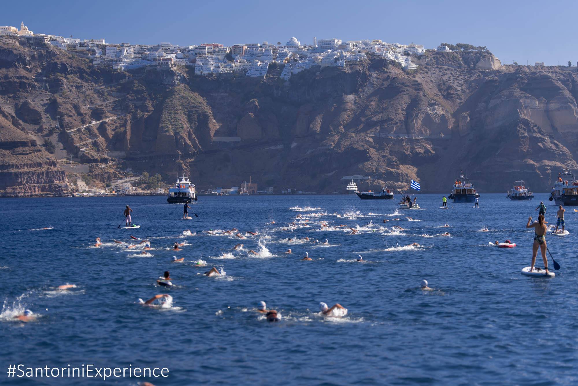 Open-water swimmers near Santorini cliffs and boats