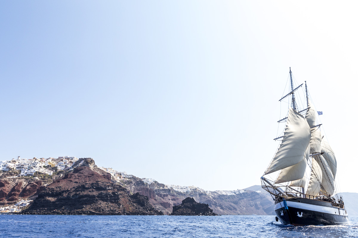 Tall sailing ship near Santorini’s white cliffside villages
