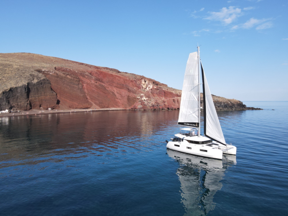 White sailboat near red rocky coastline