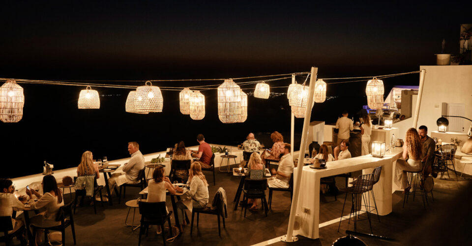 Nighttime rooftop restaurant with diners beneath woven lanterns