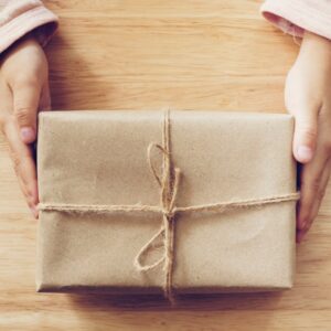 Child holding twine-wrapped gift box on wooden table
