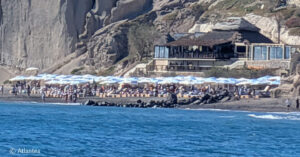Crowded beach with umbrellas beneath the rocky cliffs of Vlyhada.