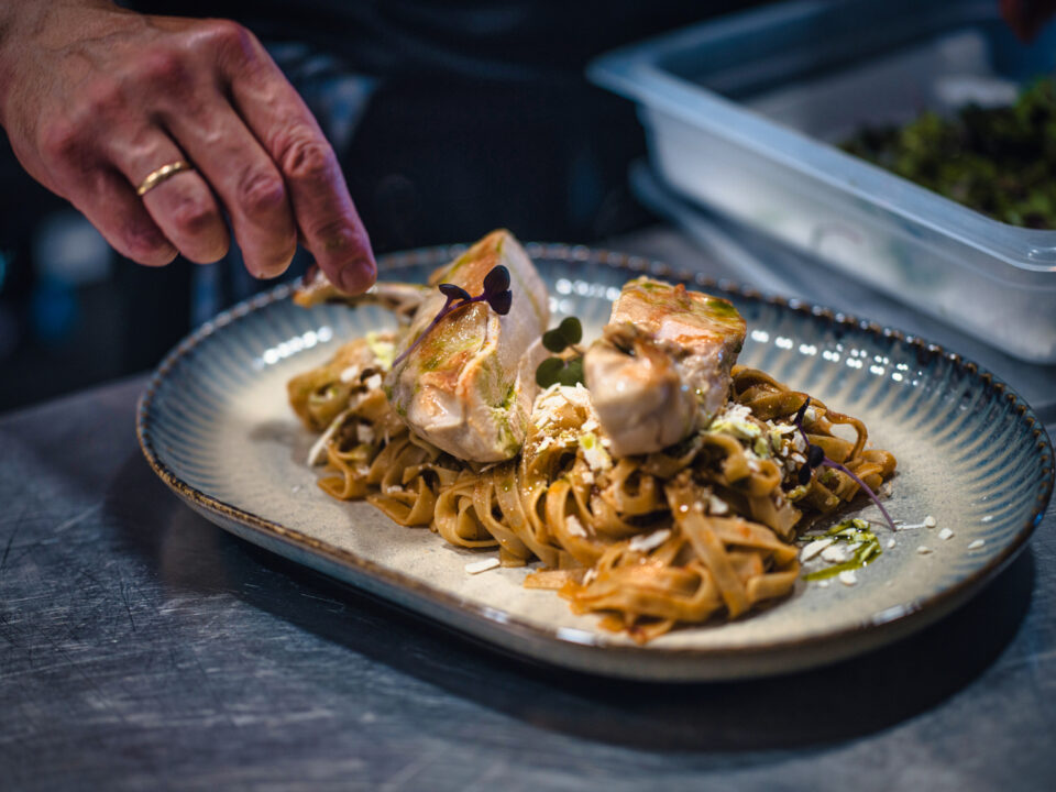 Chef garnishing salmon pasta with microgreens