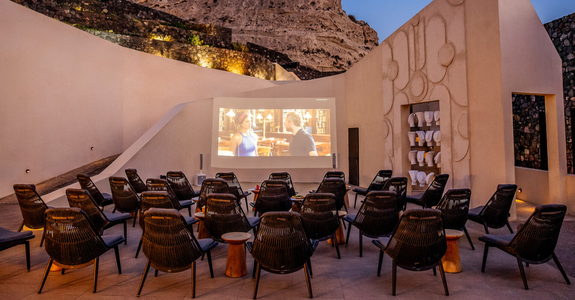 Outdoor cinema with wicker chairs beneath rocky cliff