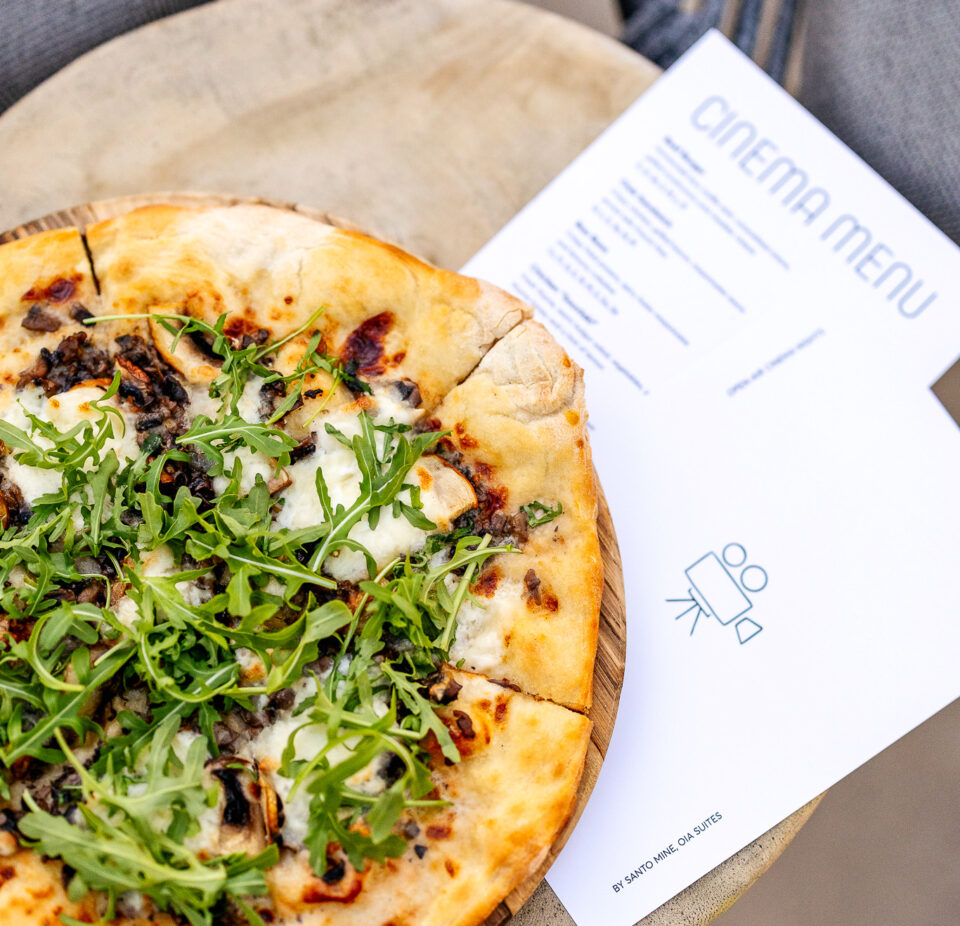Arugula and mushroom pizza beside cinema menu