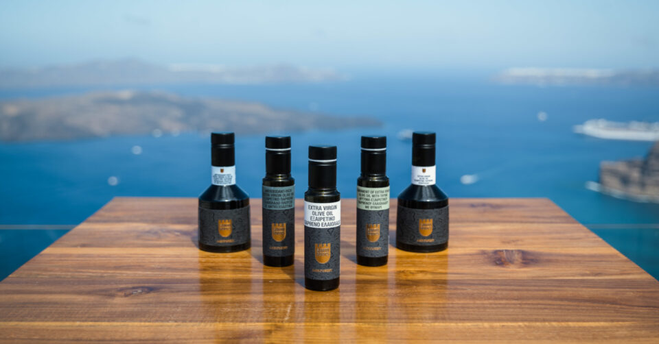 Five olive oil bottles on wooden table overlooking sea