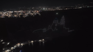 Hillside church outline illuminated above coastal city at night